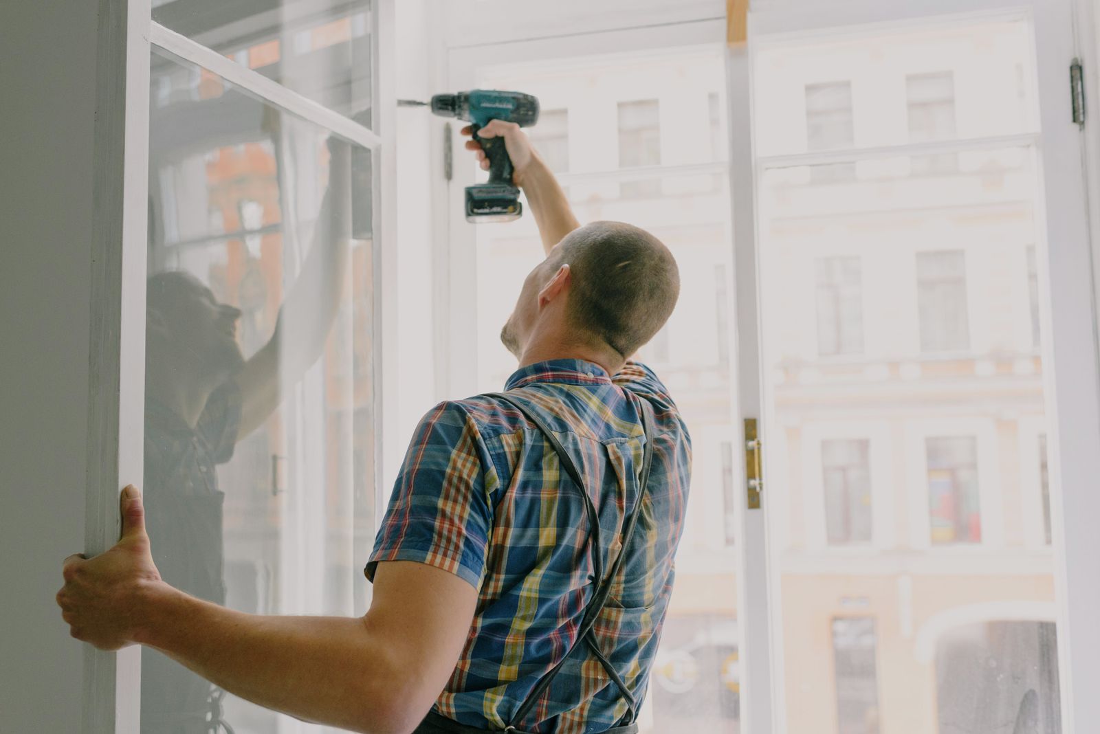 A handyman holding a window frame in place while drilling into it